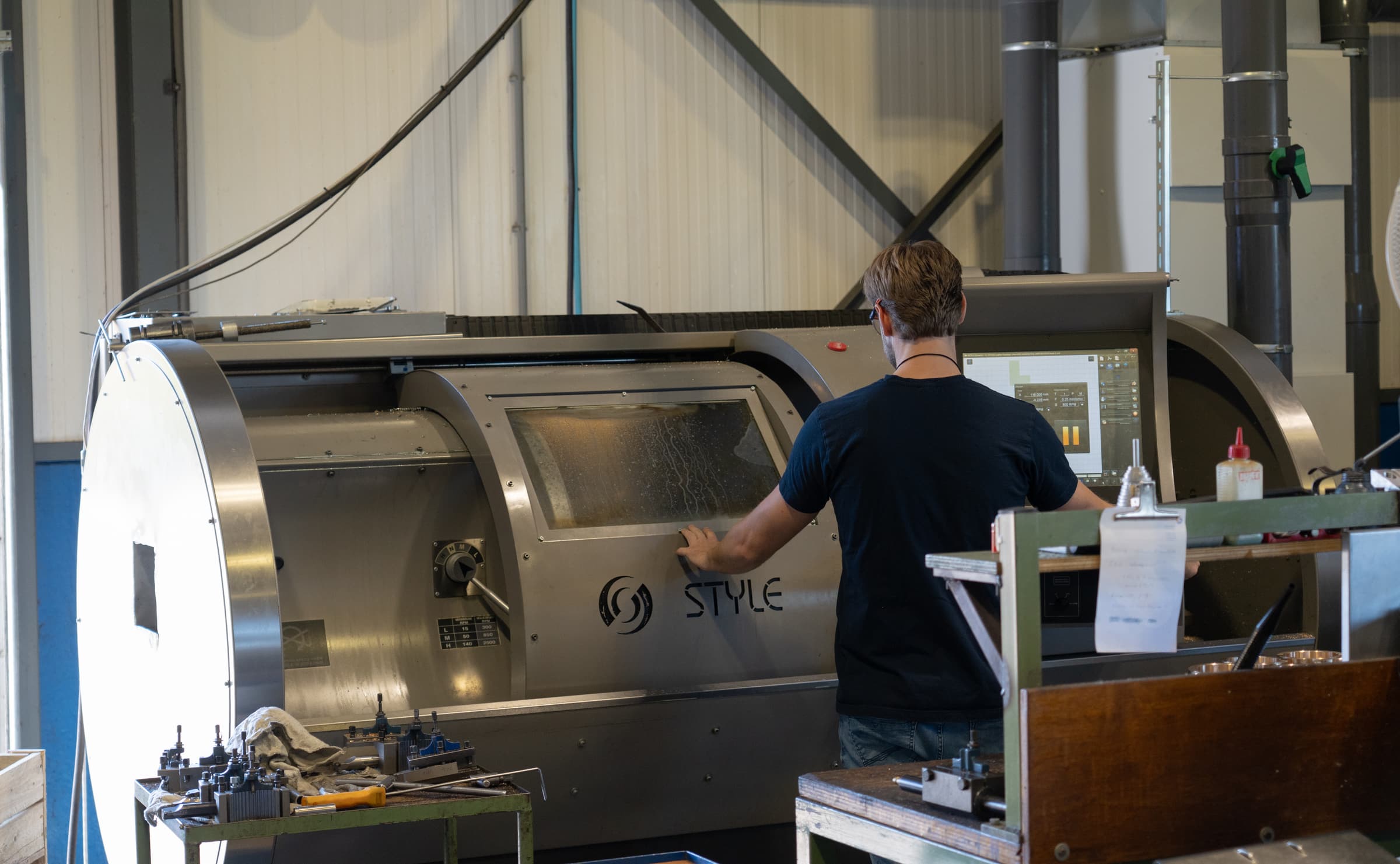 Foto: een van onze CNC-draaibanken in bedrijf, met de collega aan de besturing