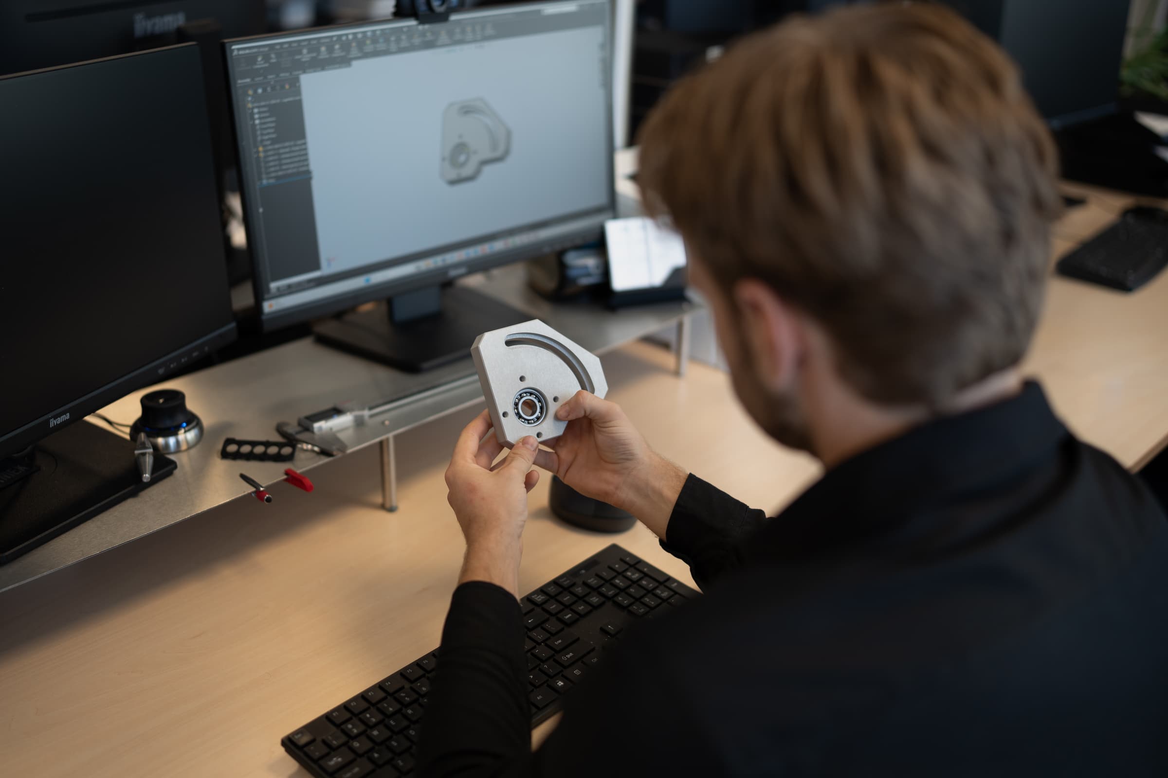 Onze engineer met het gefreesde deel in de hand en het 3D-model op het scherm